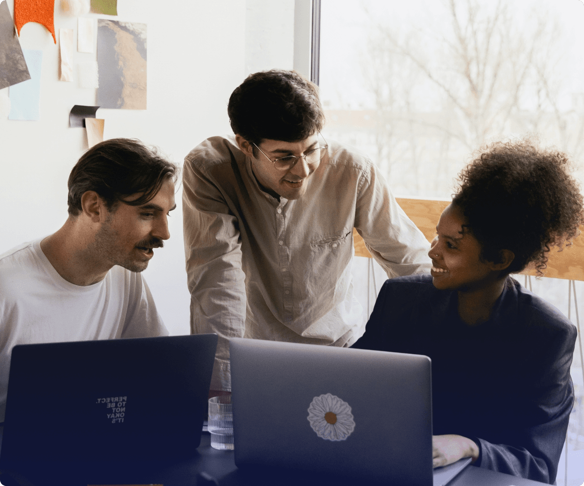 three people looking at two laptops in a casual office setting